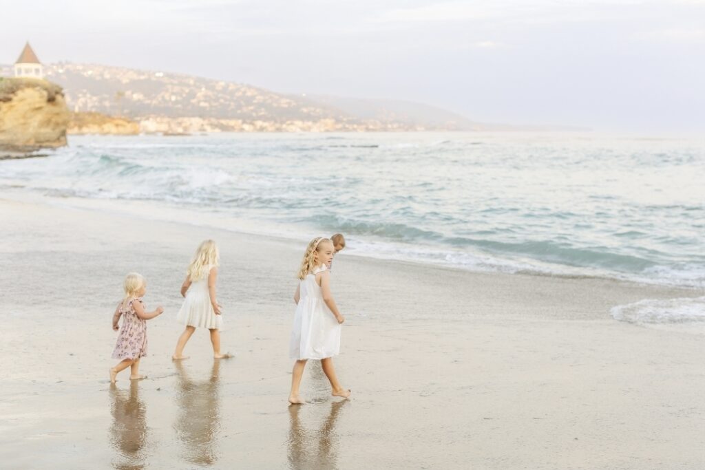 Three young children walking barefoot along the shoreline of Laguna Beach at sunset, captured in soft, golden light.
