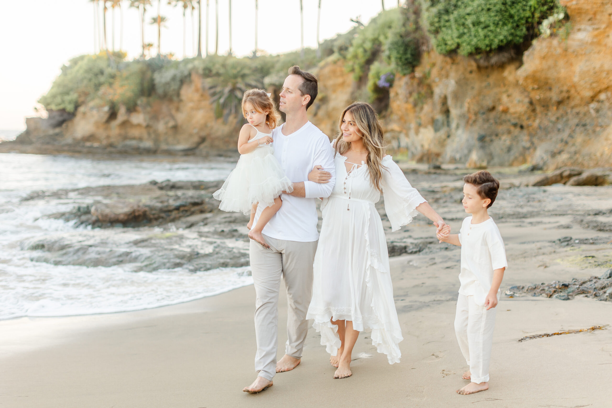 Family of four holding hands walking along the shoreline during golden hour.